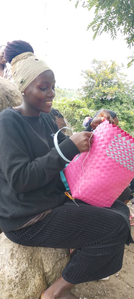 A young woman concentrates while weaving a basket.
