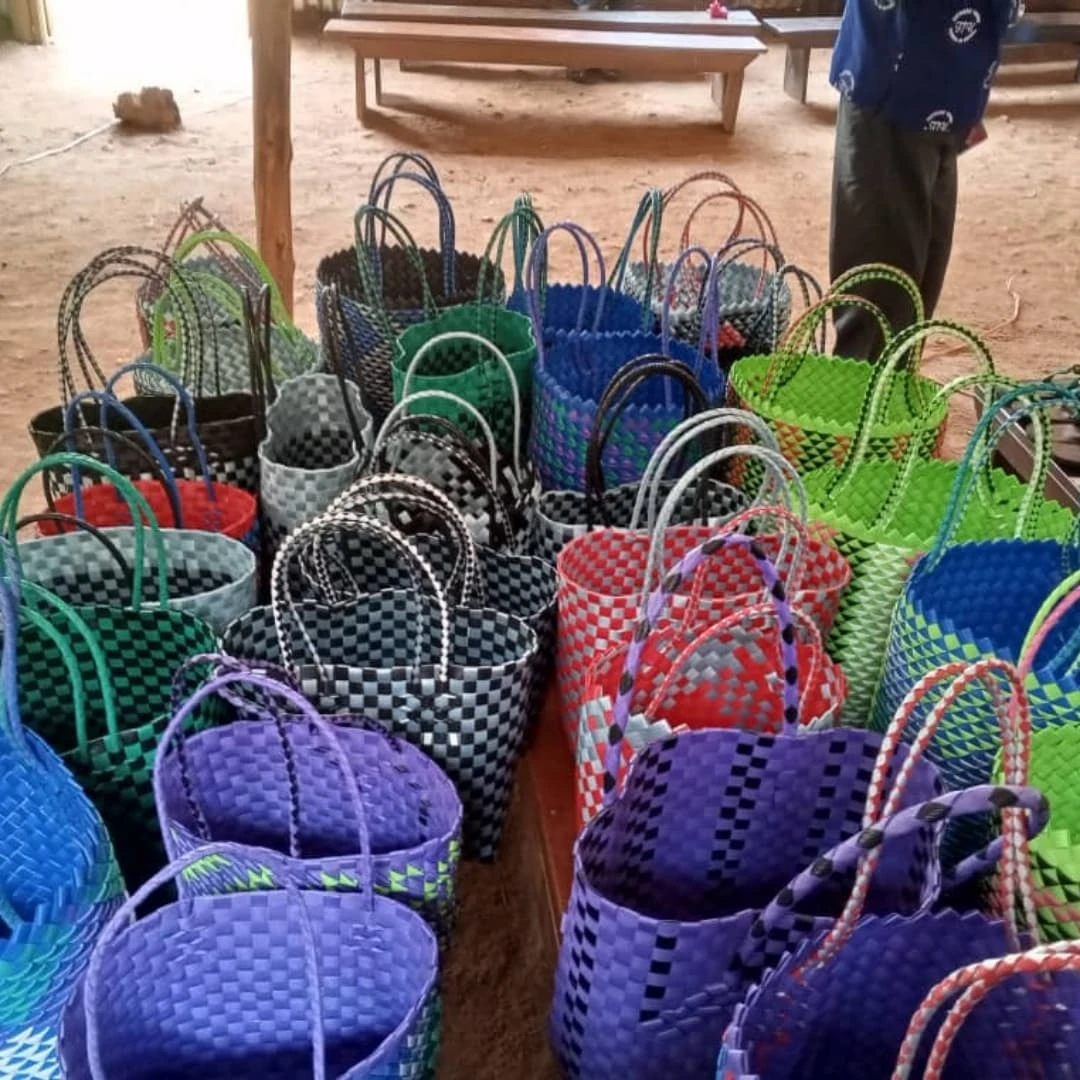 Large collection of colorful handmade woven plastic bags displayed together on tables inside a workshop or training center.